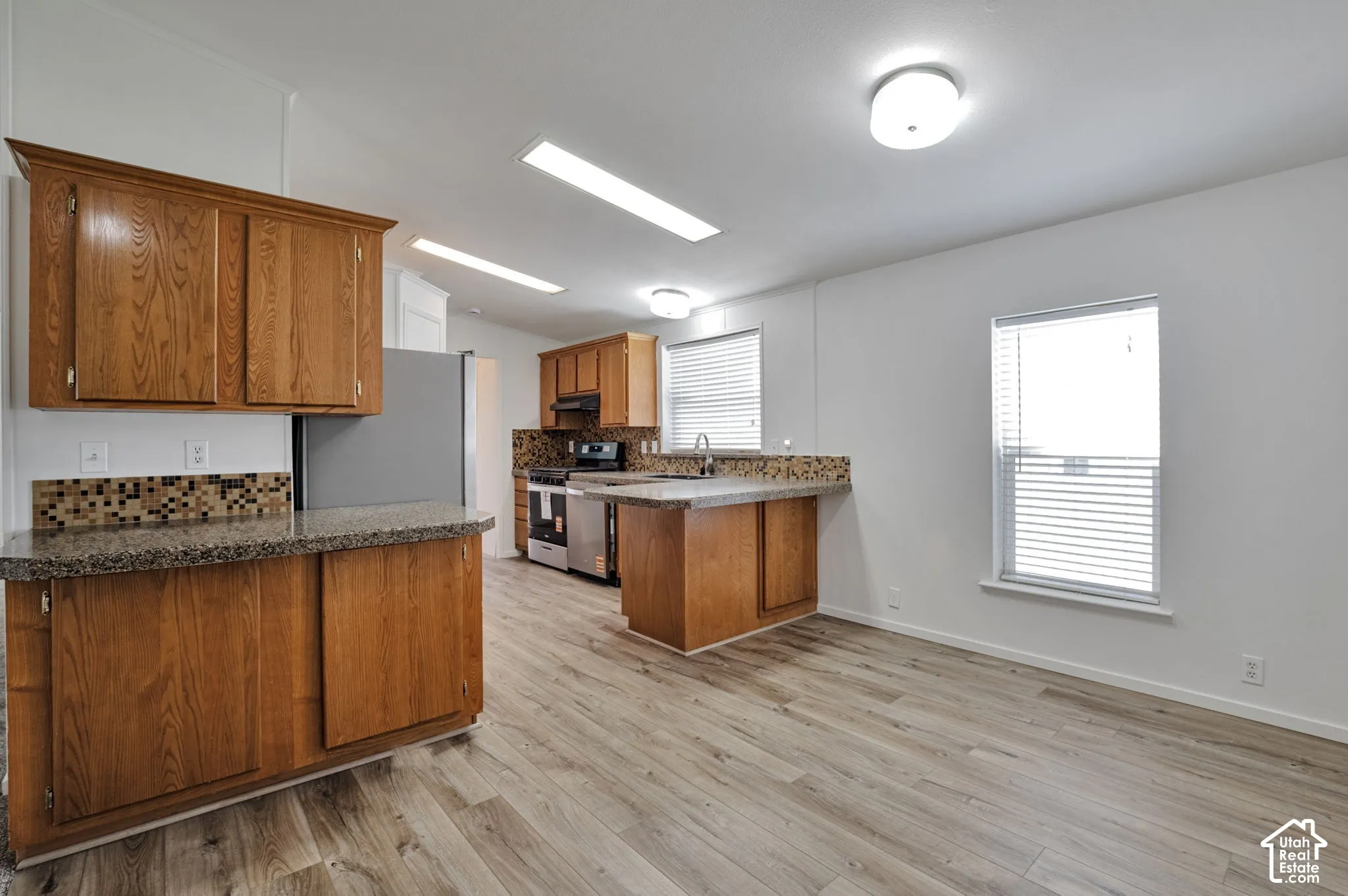 Kitchen featuring wood-finish cabinetry, speckled countertops, tile backsplash, and stainless steel appliances