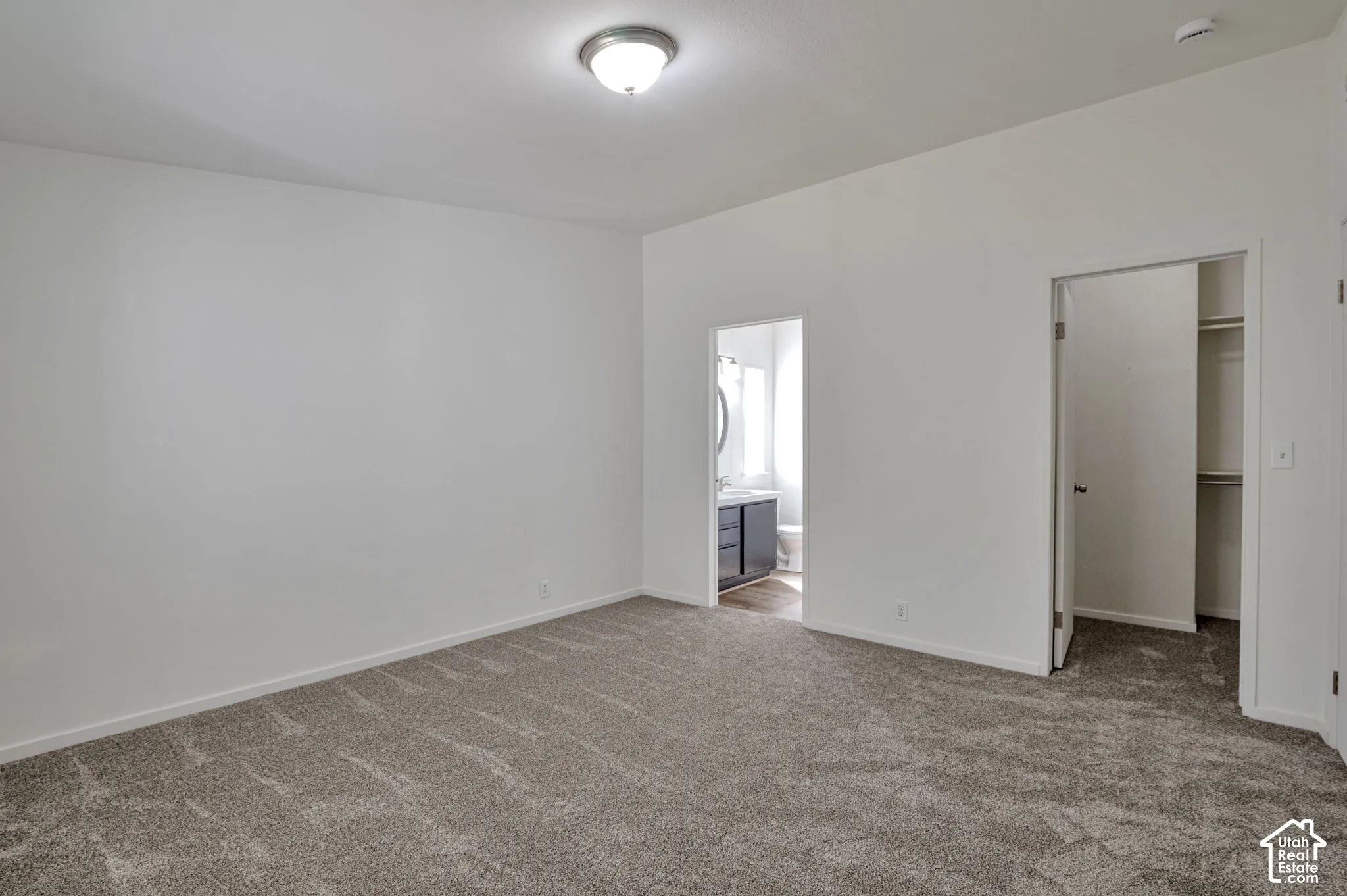 Spacious room featuring neutral carpeting, a ceiling-mounted light fixture, and a doorway to a bathroom with a modern vanity