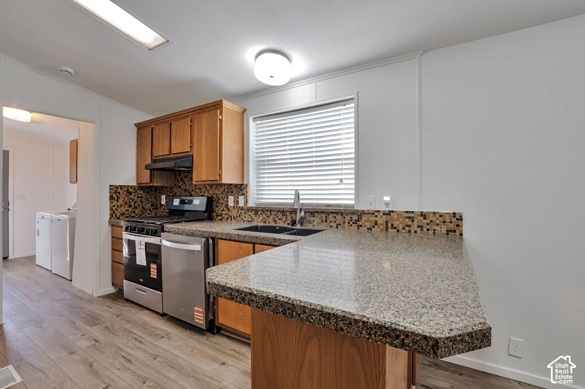 Kitchen featuring wood-finish cabinetry, stainless steel appliances, mosaic tile backsplash, and composite countertops