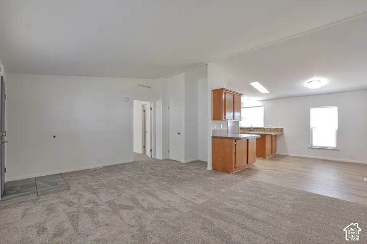 Open-concept living space with carpeted flooring, wood-finish cabinetry, and a kitchen peninsula with a stone-look countertop