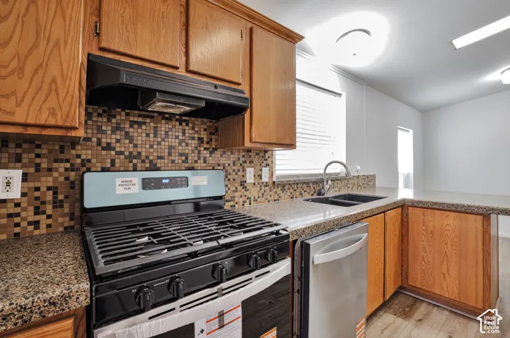 Kitchen featuring wood cabinetry, granite-style countertops, mosaic tile backsplash, a stainless steel dishwasher, and a gas range