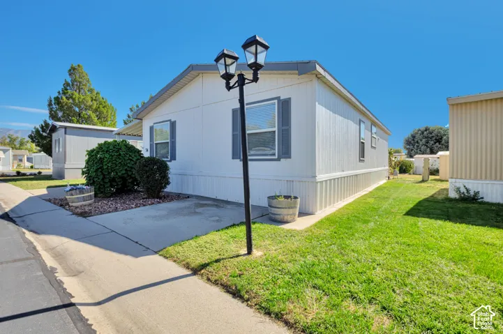 White exterior siding with dark window shutters, concrete walkway, street lamp, and a grass lawn