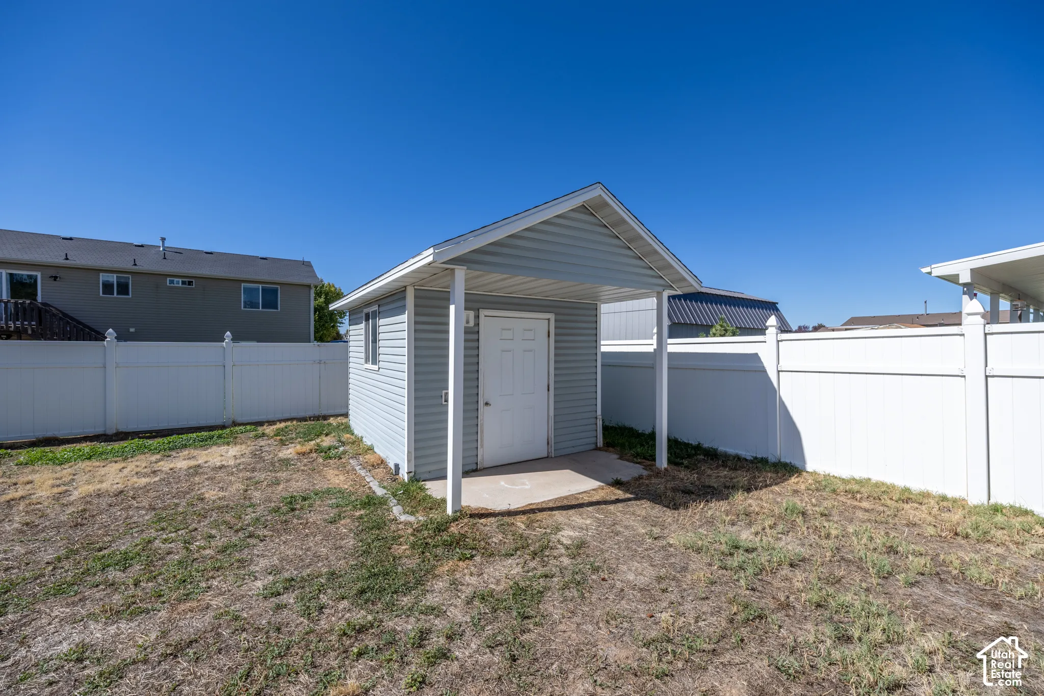 Detached shed with light gray vinyl siding and a covered entry. This shed has its own electric panel and power.