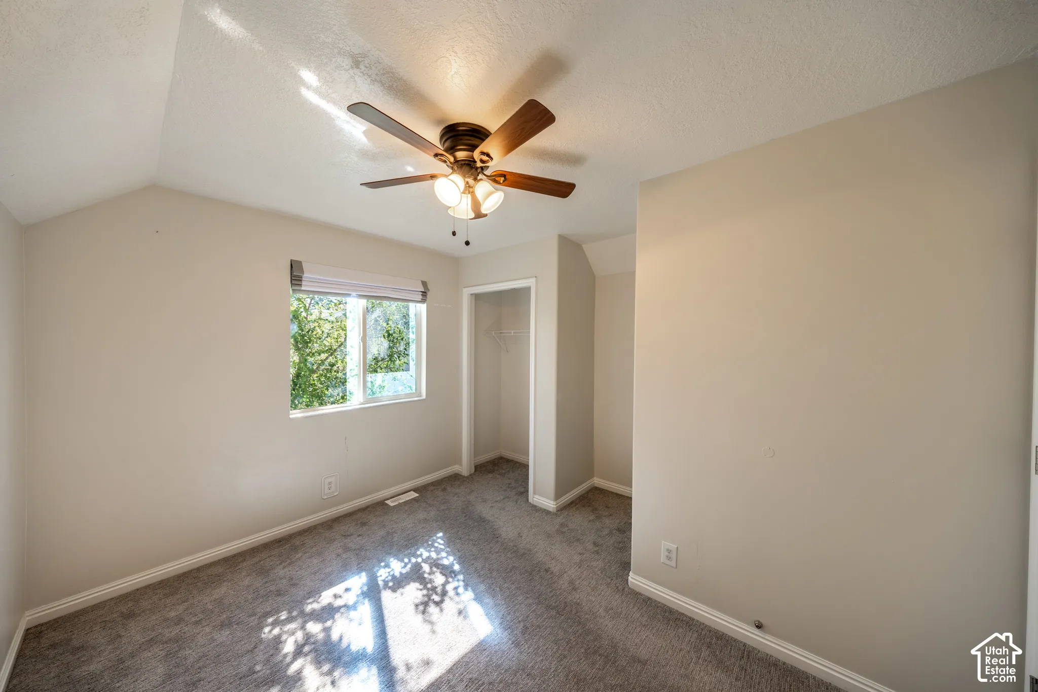 Bedroom #4 on 2nd floor. Vaulted ceiling, ceiling fan with integrated lighting, window with a roller shade, neutral-toned carpeting, and a built-in closet