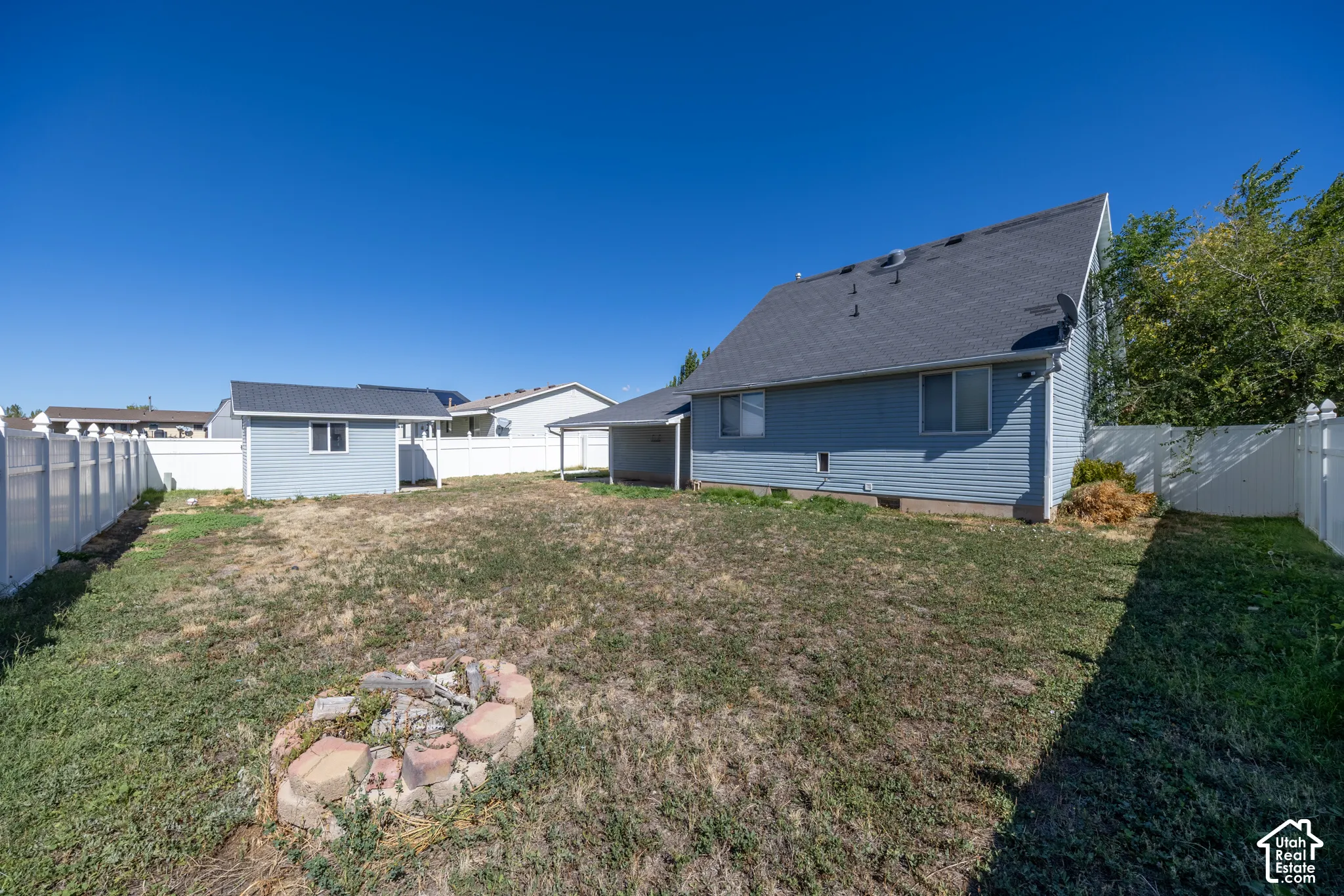 Expansive backyard with a dedicated fire pit area, fully enclosed by a white privacy fence