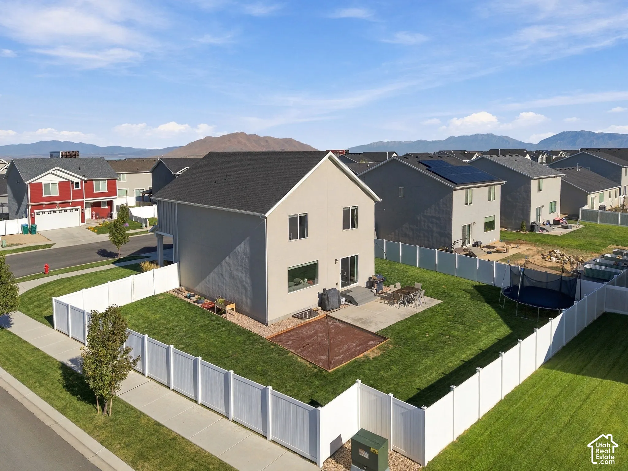 Expansive backyard featuring a manicured lawn, white privacy fencing, and a concrete patio