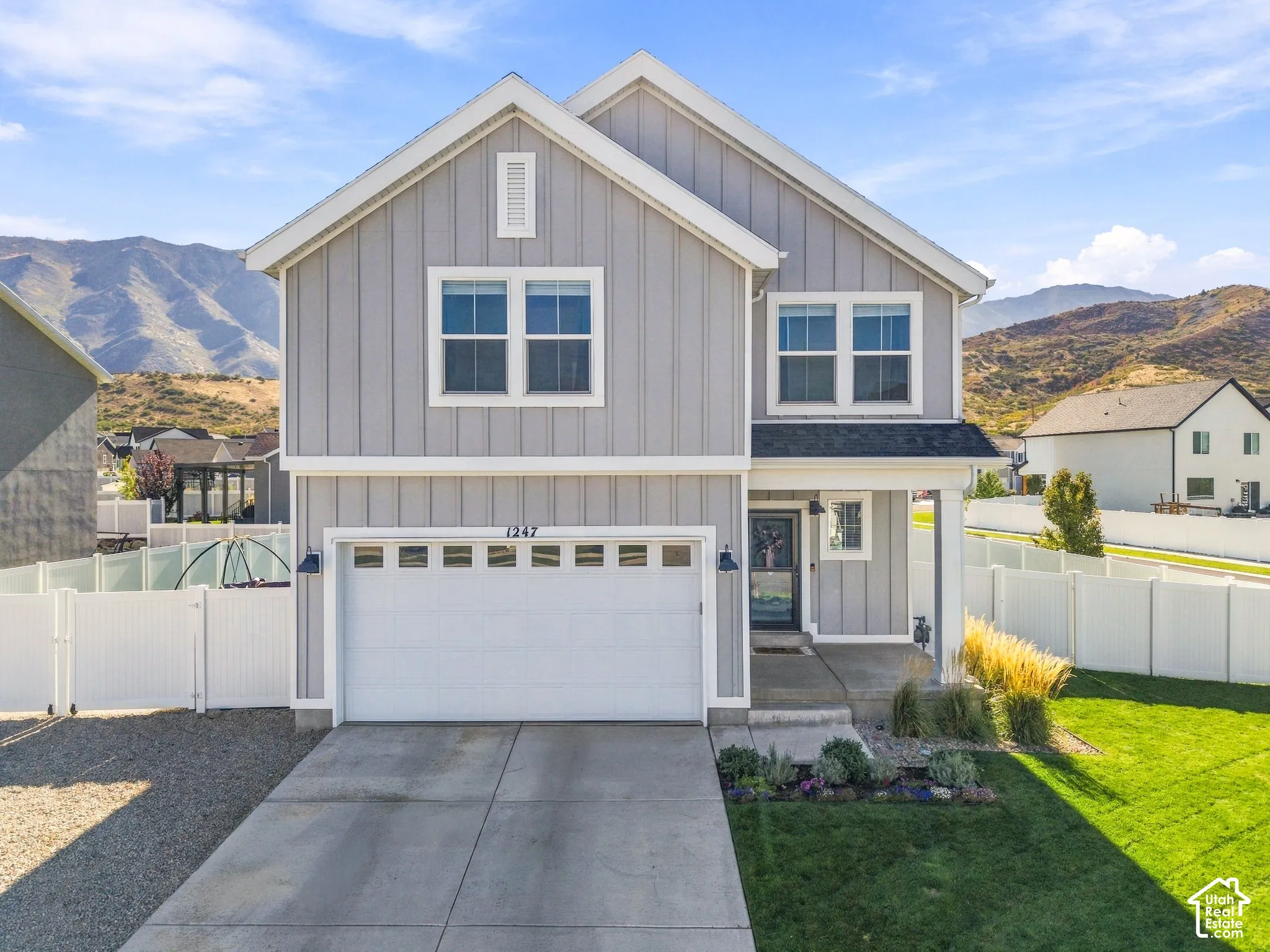 Grey board and batten siding, white trim accents, attached two-car garage, covered porch entry, and a front lawn