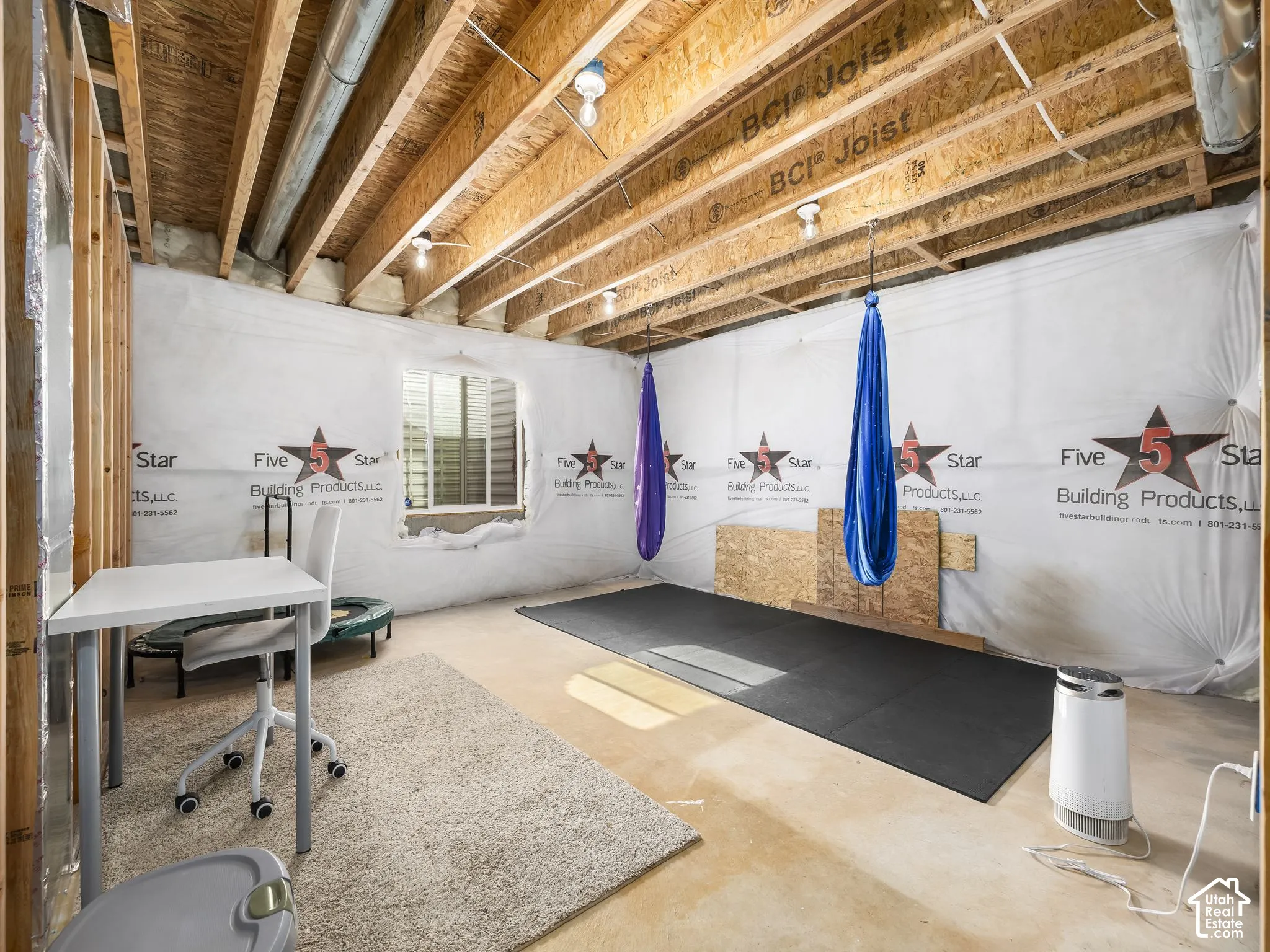 Unfinished basement space with exposed wood joists, structural framing, and a window with blinds