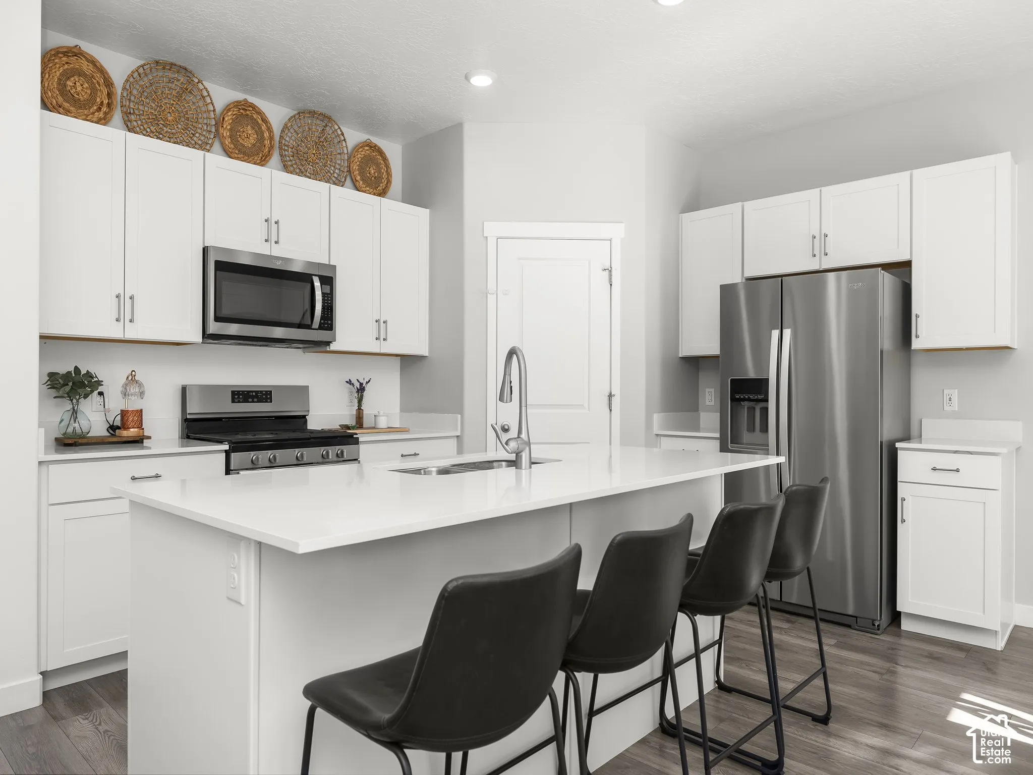 White cabinetry with brushed nickel hardware, stainless steel appliances, a center island with countertop seating, a stainless steel sink with a high-arch faucet, and wood-finish flooring