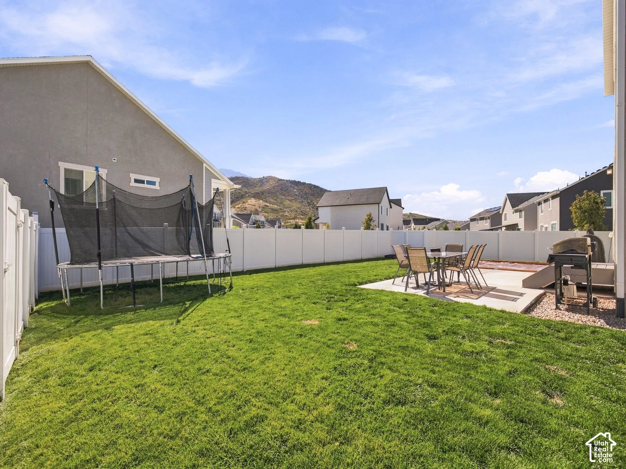 Expansive green lawn with a concrete patio, privacy fencing, and distant mountain scenery