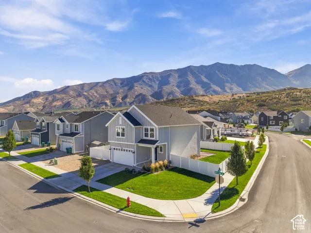Modern residential architecture with mountain backdrop, featuring a manicured lawn, paved sidewalks, and a two-car garage