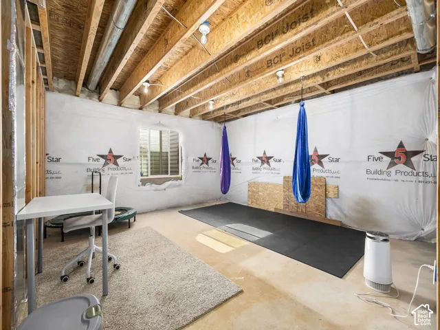 Unfinished basement space with exposed wood joists, structural framing, and a window with blinds