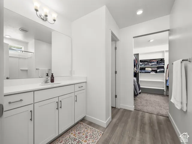 Bathroom featuring a wide vanity with a single basin, ample white cabinetry, and a large mirror