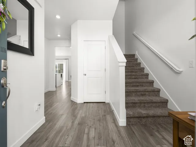 Entryway featuring wood-finish flooring, recessed lighting, white trim, and a carpeted staircase with a white handrail