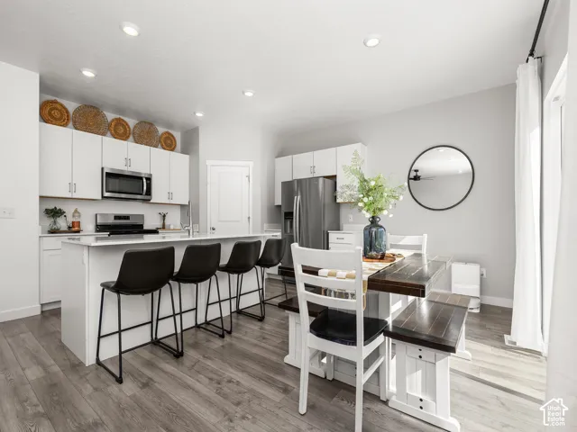 Open-concept kitchen and dining area featuring recessed lighting, white cabinetry, stainless steel appliances, a kitchen island, and wood-finish flooring