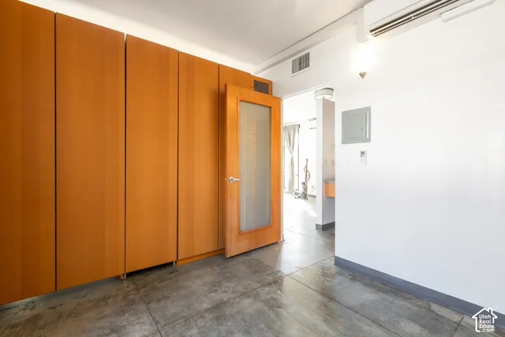 Built-in wood-finish cabinetry, wood-finish door with frosted glass panel, concrete flooring, and wall-mounted air conditioning unit
