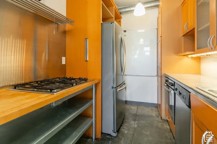 Galley kitchen featuring wood-finish cabinetry, stainless steel appliances, a gas cooktop, and built-in oven