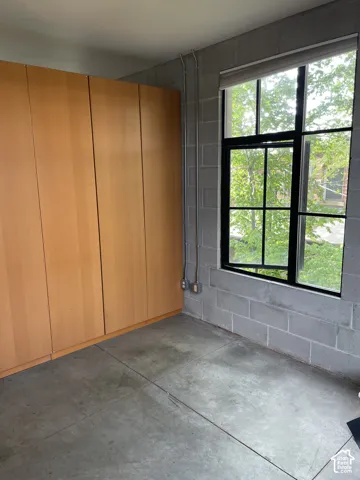 Built-in cabinetry with wood-finish doors, exposed concrete block wall, concrete flooring, and a large multi-pane window