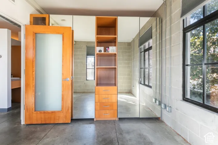 Polished concrete flooring, exposed concrete block walls, large industrial-style windows, full-height mirrored closet doors, and a built-in wood-finish shelving unit