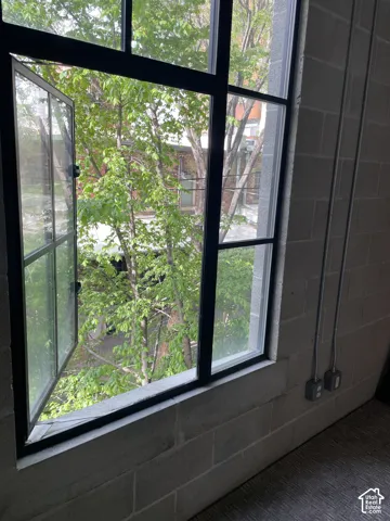 Black-framed industrial-style window with an operable casement pane, set within a concrete block wall