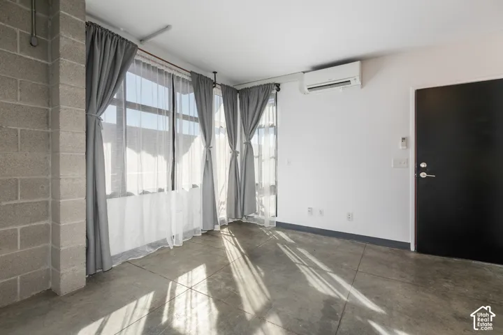 Exposed concrete block wall, polished concrete flooring, large window banks, white walls, and a wall-mounted mini-split HVAC unit
