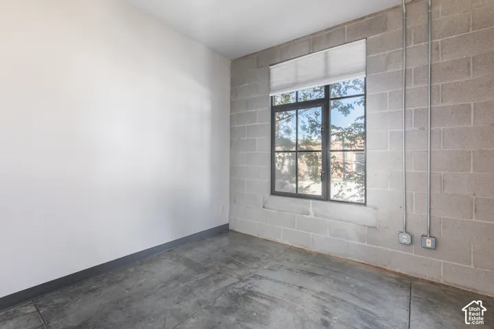 Polished concrete flooring, exposed concrete block wall, industrial conduit, large grid-pane window, and roller shade