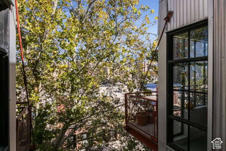 Exterior balcony with metal railings, featuring a large pane window with dark framing and corrugated metal siding