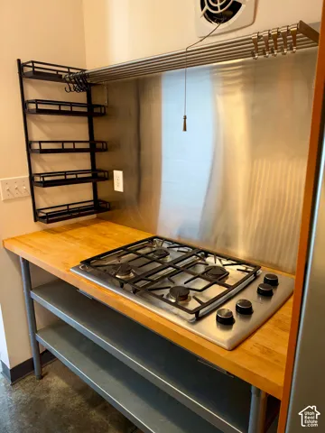 Stainless steel gas cooktop, wood-finish countertop, stainless steel backsplash, and metal shelving
