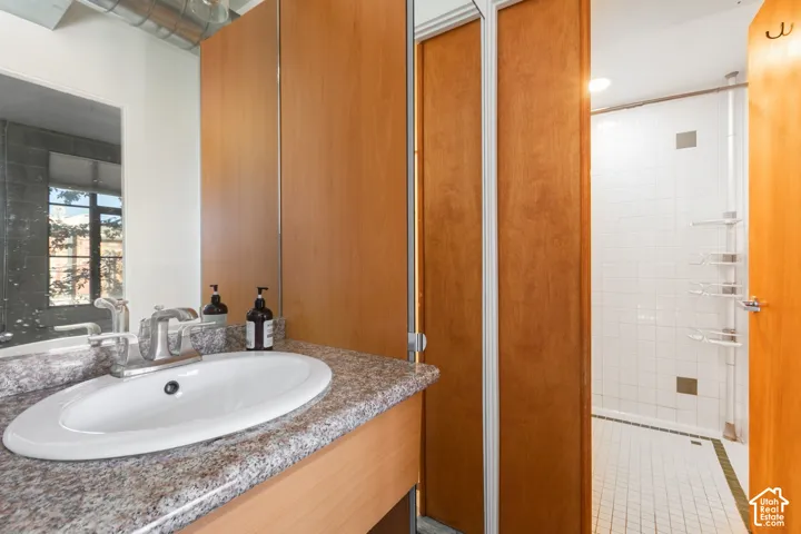 Vanity with an integrated sink and stone-finish countertop, wood-finish cabinetry, and a fully tiled shower with a sliding door