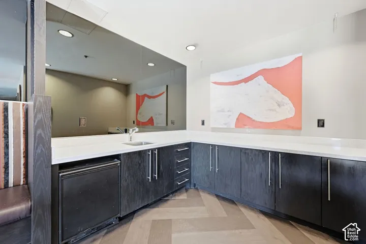 Spacious Owner lounge featuring dual vanities with white quartz countertops, dark cabinetry with brushed metal hardware, recessed lighting, and a geometric wood-finish floor