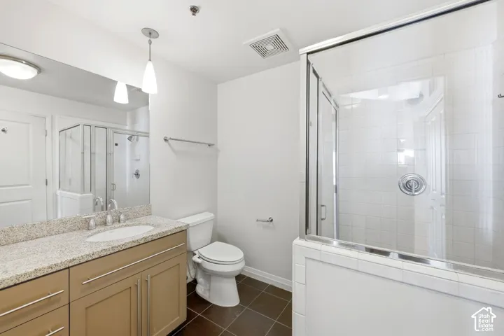 Glass-enclosed shower with white subway tile, single vanity with a light-toned countertop, integrated sink, and modern pendant lighting