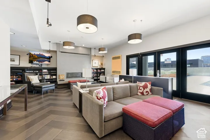 Spacious Owner lounge area featuring herringbone wood-finish flooring, built-in shelving, a modern linear fireplace, and large glass panel doors opening to an outdoor patio