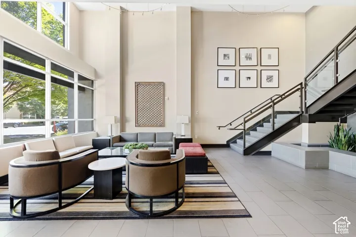 Two-story ceiling height, expansive window wall, light-toned wall finishes, open-tread staircase with glass railing, and large format tile flooring