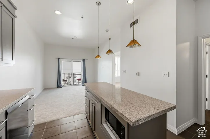 Kitchen island with stone-finish countertop, recessed lighting, tile flooring, and sliding glass door to balcony