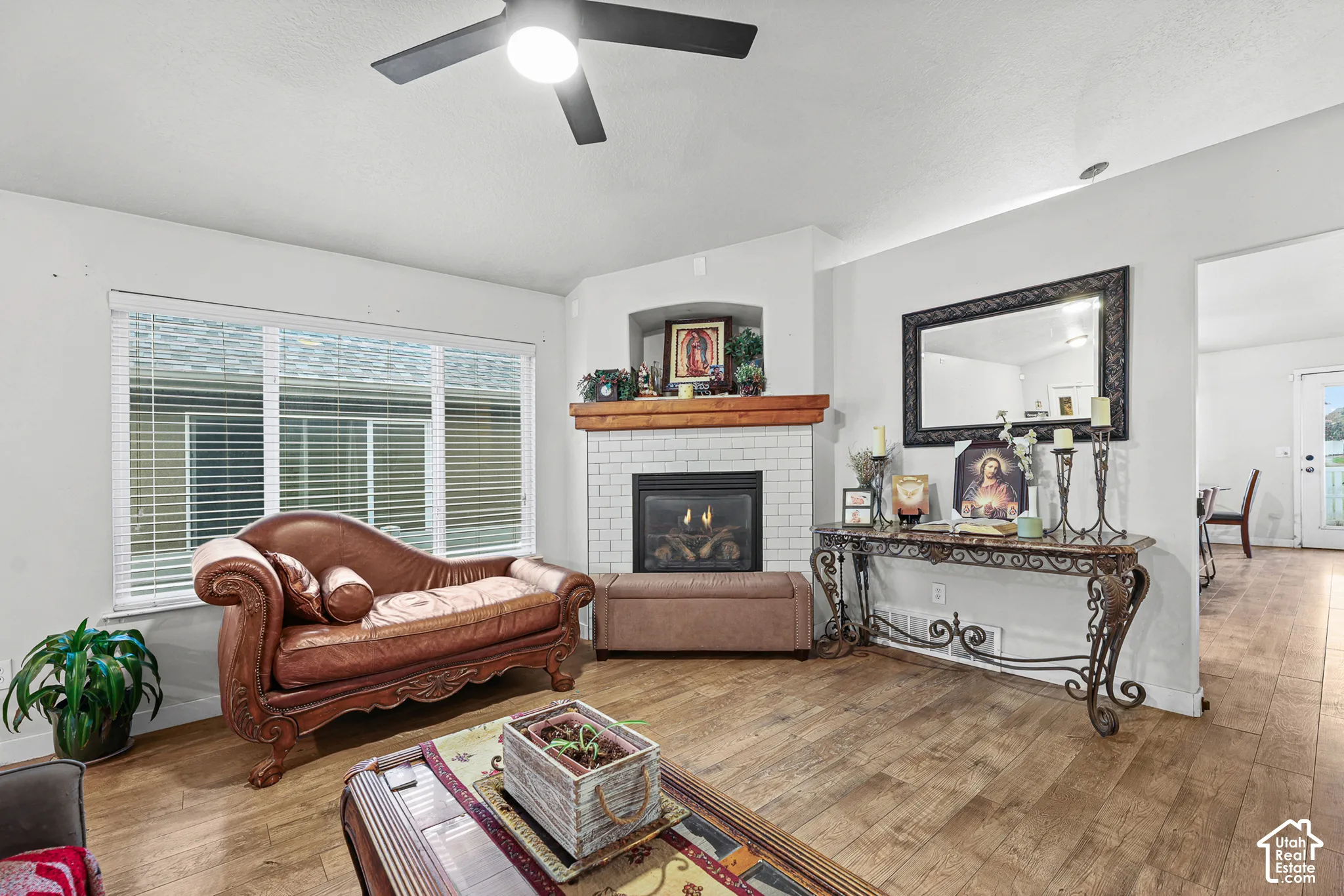 Living space featuring wood-finish flooring, a corner fireplace with white subway tile surround, a wood mantel, and an overhead ceiling fan