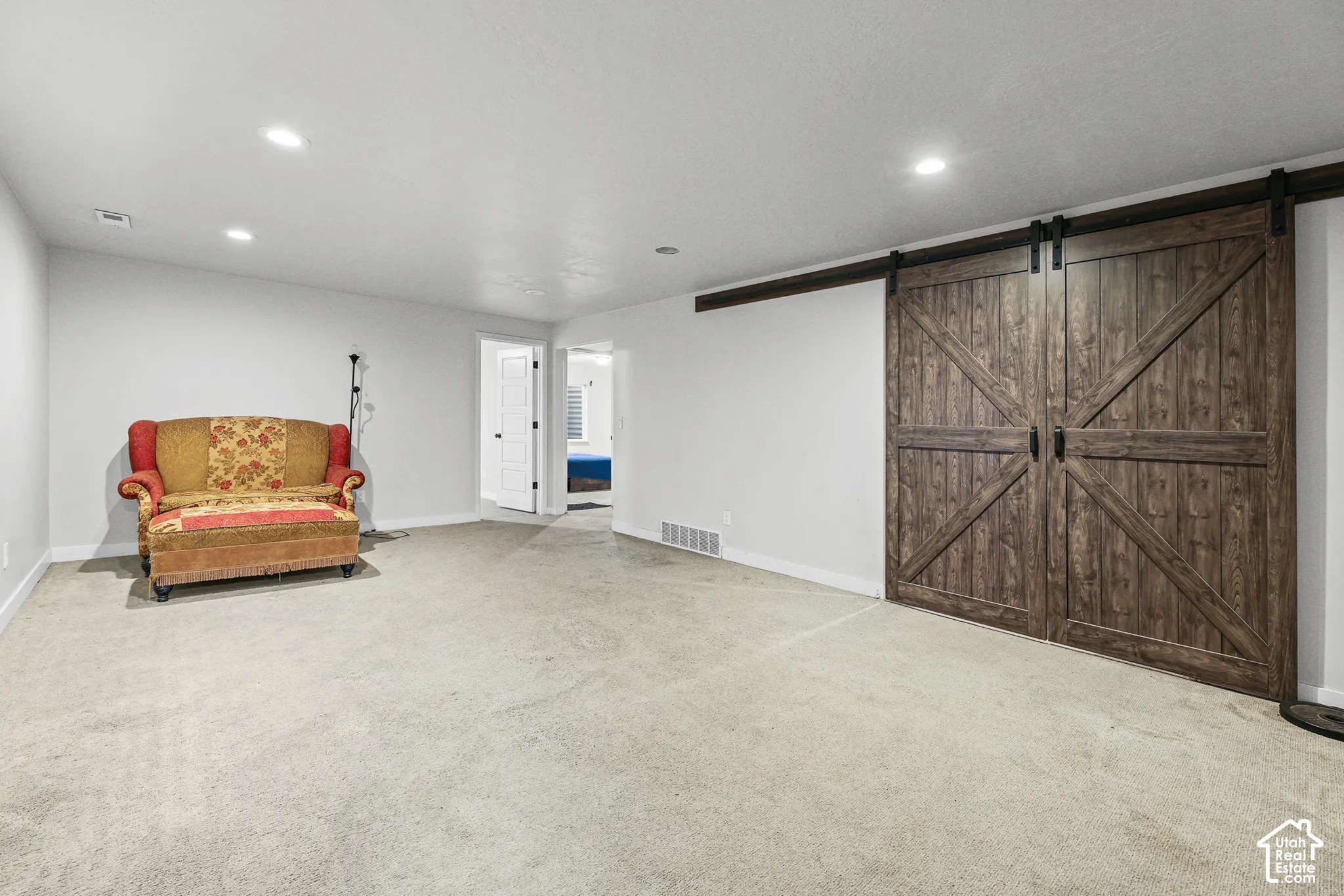 Spacious room featuring light-colored carpet, recessed lighting, and a double barn door with dark hardware