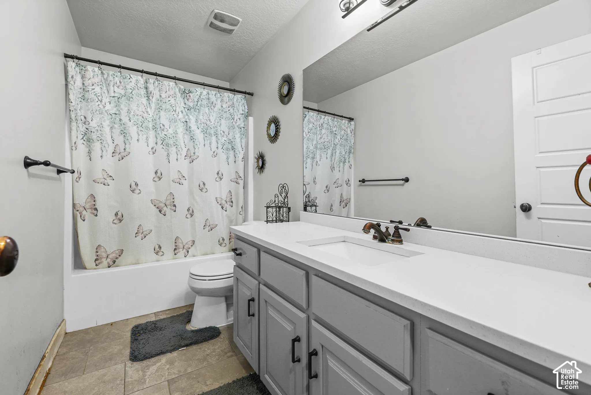 Vanity with integrated sink and bronze-finish hardware, expansive wall-mounted mirror, and tile flooring
