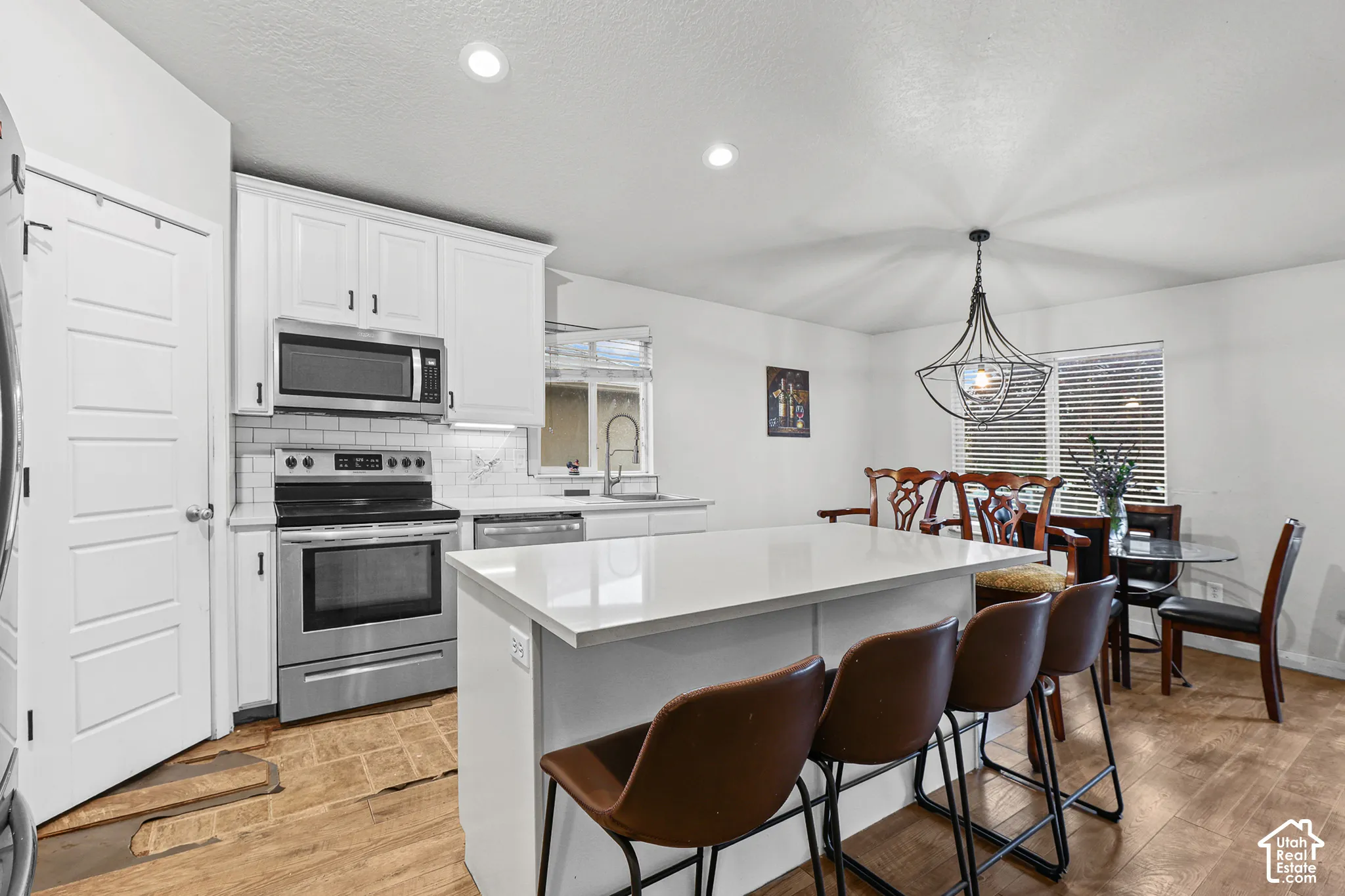 Kitchen featuring white shaker cabinetry, stainless steel appliances, a white tile backsplash, and wood-finish flooring