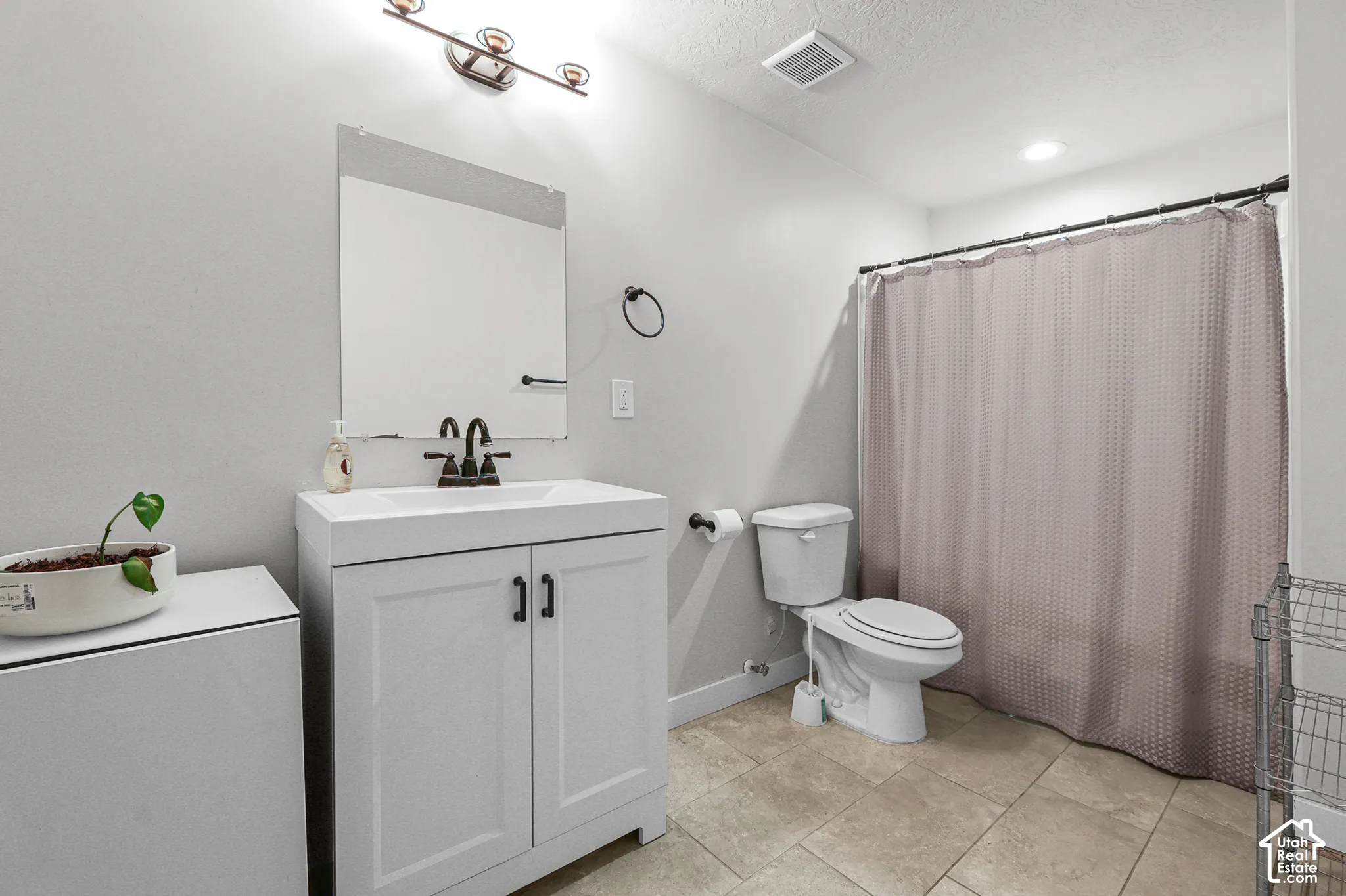 White vanity with integrated sink, bronze-finish faucet, framed mirror, and tiled flooring