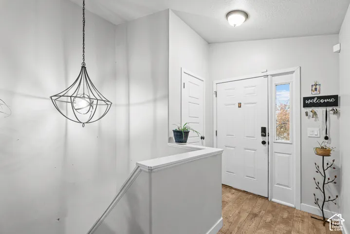 Entryway featuring wood-finish flooring, a contemporary hanging light fixture, a white paneled front door, and a sidelight window