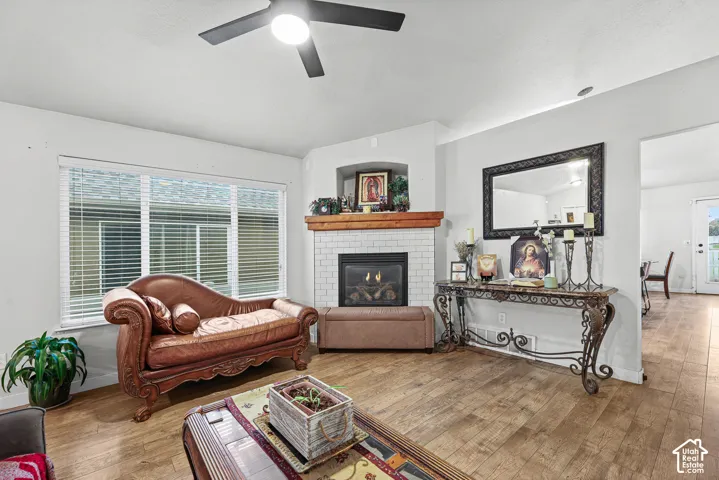 Living space featuring wood-finish flooring, a corner fireplace with white subway tile surround, a wood mantel, and an overhead ceiling fan