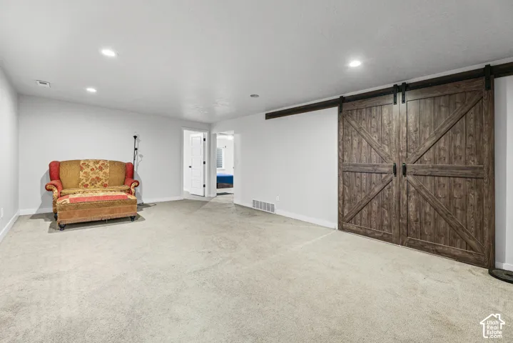 Spacious room featuring light-colored carpet, recessed lighting, and a double barn door with dark hardware