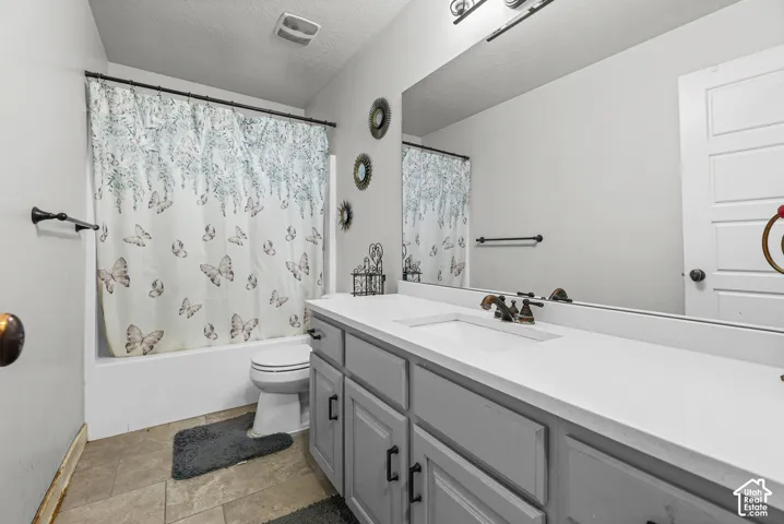 Vanity with integrated sink and bronze-finish hardware, expansive wall-mounted mirror, and tile flooring