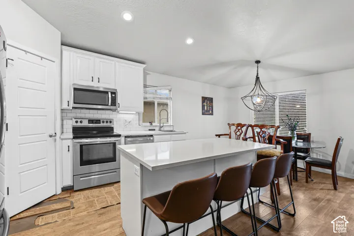 Kitchen featuring white shaker cabinetry, stainless steel appliances, a white tile backsplash, and wood-finish flooring