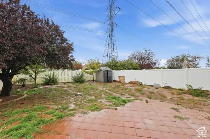 Spacious backyard featuring a brick paver patio, a white privacy fence, mature trees, and a storage shed