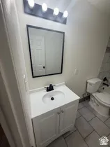 White vanity with cabinet storage, black hardware, black framed mirror, and rectangular floor tiles