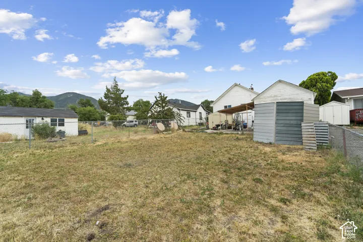 Expansive lot featuring a chain-link fence, two utility sheds, and mature trees