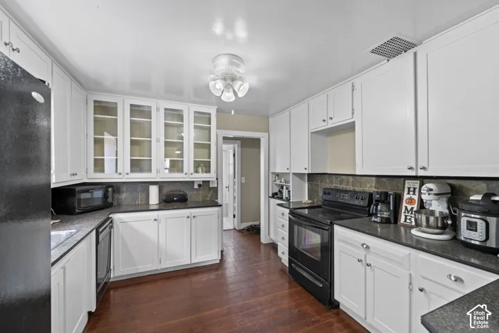 White cabinetry with glass-front uppers, dark countertops, tile backsplash, and wood-finish flooring