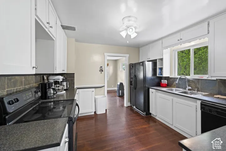 Kitchen with wood-finish flooring, white cabinetry, black countertops, tile backsplash, and a double-basin stainless steel sink
