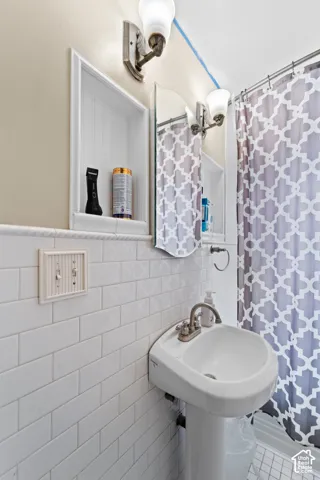 Pedestal sink with a dual-handle faucet, subway tile wainscoting, built-in shelving, and wall-mounted lighting fixtures
